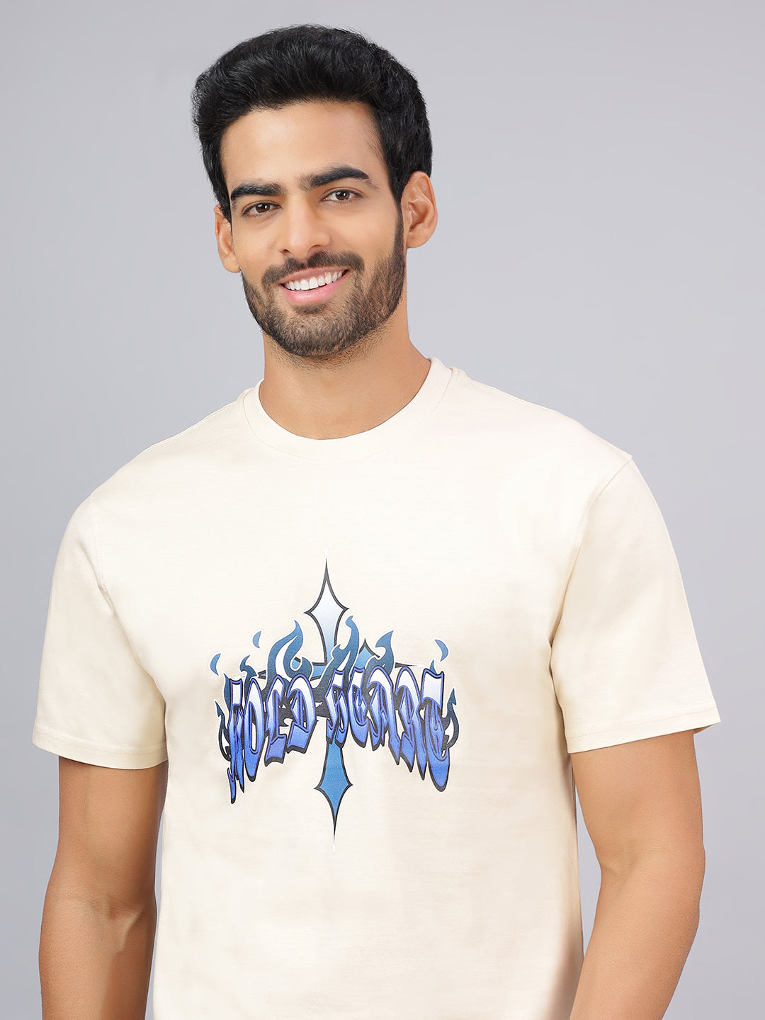 Man wearing a beige t-shirt with blue graphic design on a gray background