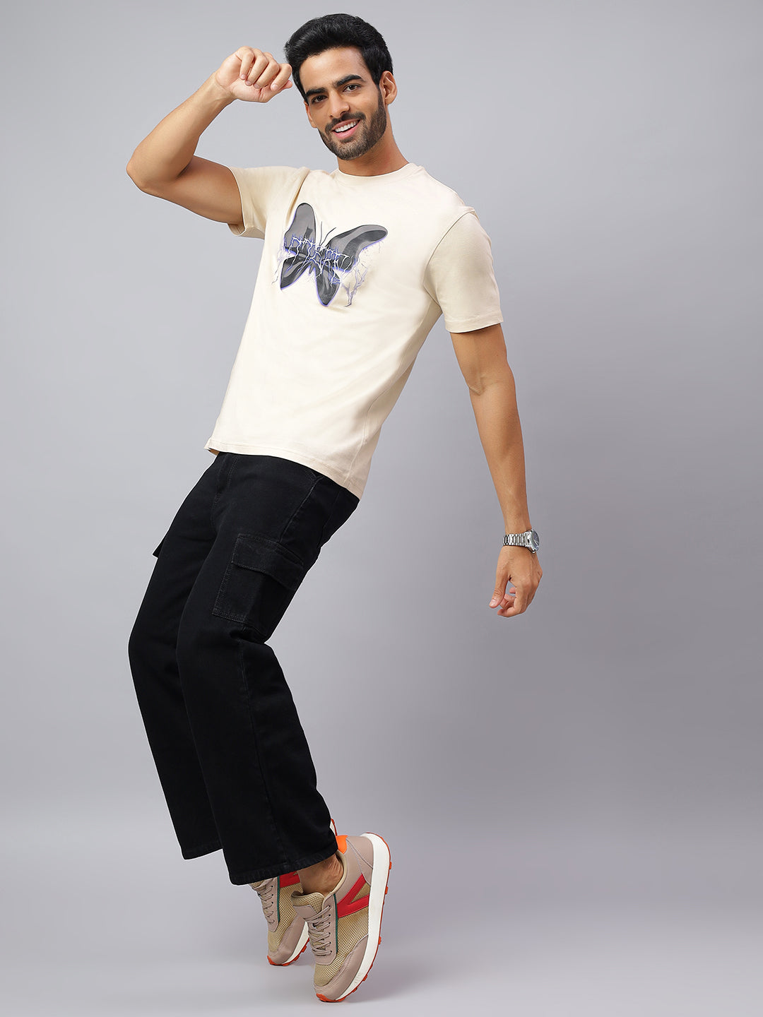 Man wearing a beige t-shirt with a butterfly design and black pants on a gray background