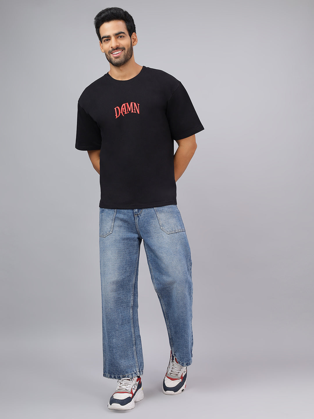 Man wearing a black t-shirt with 'DAMN' text and blue jeans on a gray background