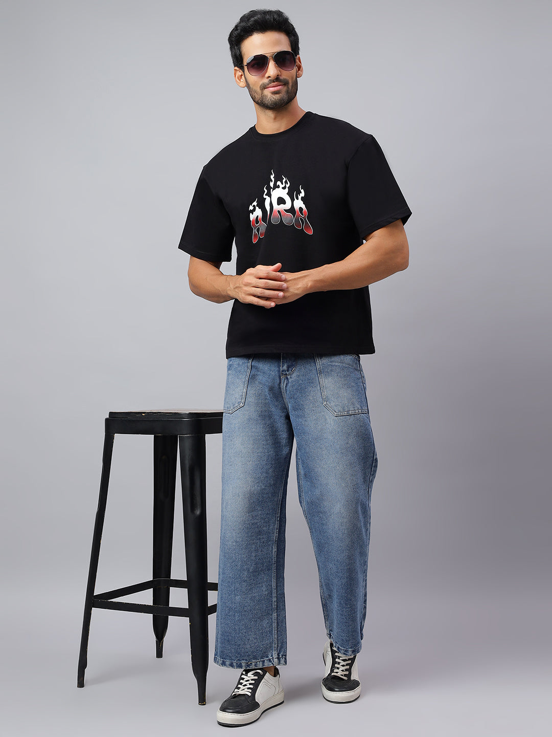 Man wearing a black t-shirt with a graphic design and blue jeans on a gray background