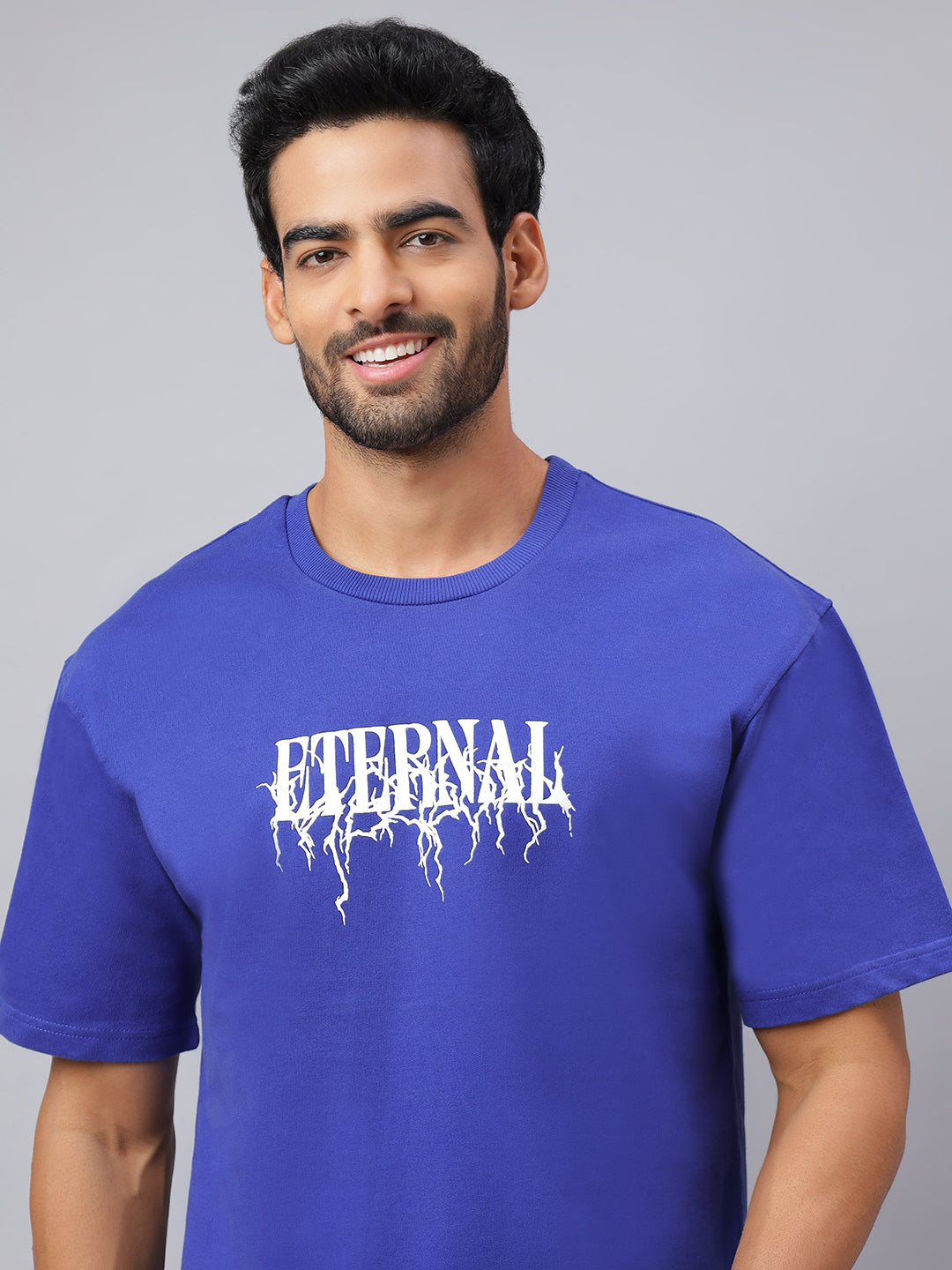 Man wearing a blue t-shirt with 'Eternal' printed on it against a gray background