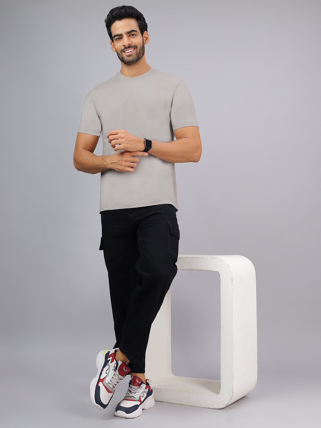 Man wearing a gray t-shirt and black pants standing next to a white stool on a gray background